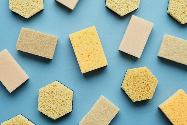 Sponges for cleaning of different shapes with a light-colored surface are randomly laid out on a blue surface